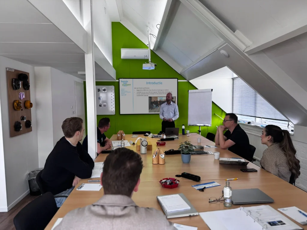Een groep mensen volgt een beheerderstraining in een moderne vergaderruimte met groene accenten.