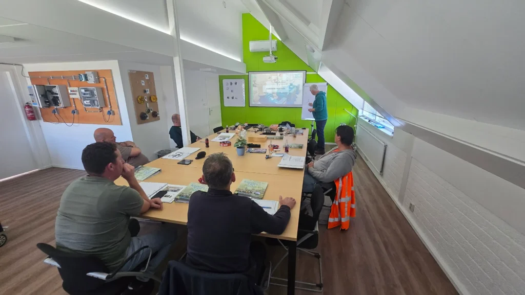 Een groep mannen volgt een technische cursus over elektrische installaties in een lichte vergaderruimte.