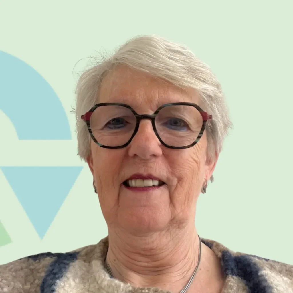 Portret van een oudere vrouw met kort, grijs haar en een bril tegen een lichtgroene achtergrond.