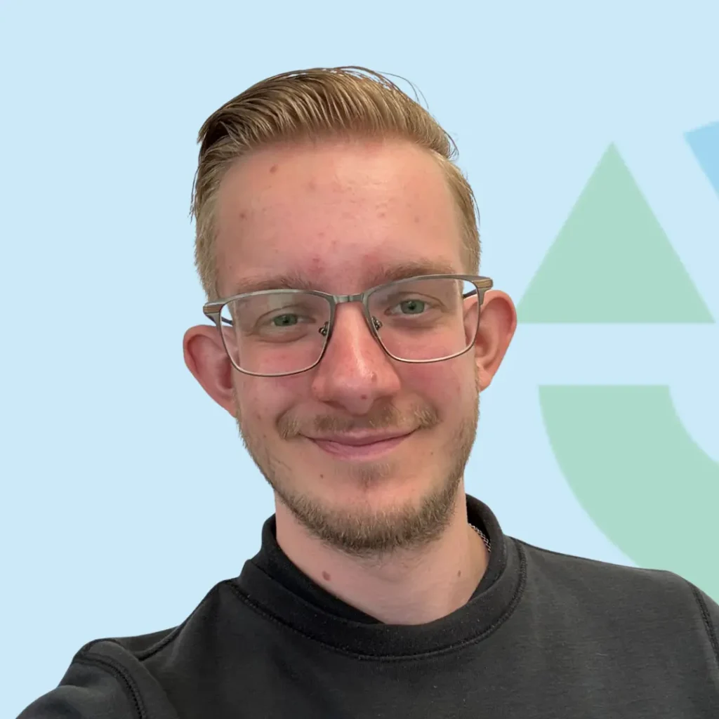 Portret van een jongeman met bril en baard tegen een blauwe achtergrond.