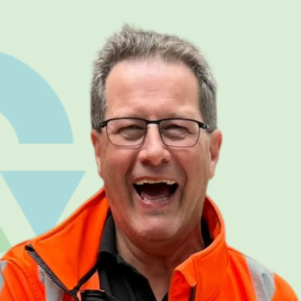 Een lachende man in een feloranje werkjas tegen een lichte achtergrond.