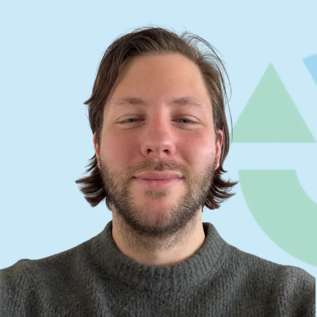 Een man met een baard en halflang haar poseert voor een lichte achtergrond met abstracte vormen.