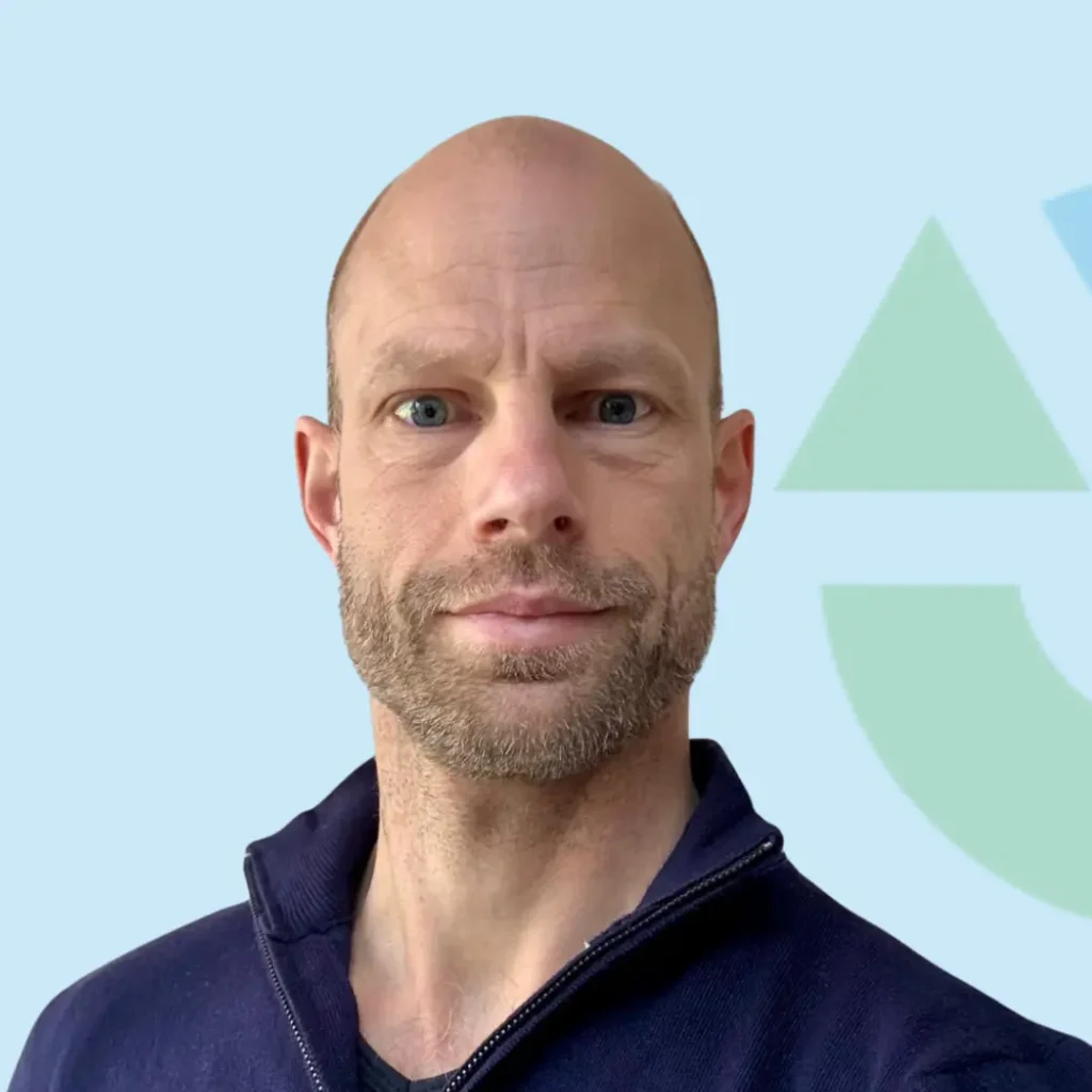 Portret van een man met een lichte baard en een navy trui voor een neutrale achtergrond.