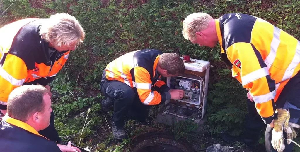 Groep medewerkers in oranje veiligheidsjassen volgt een basistraining bij een technische installatie in een groene omgeving.
