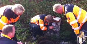 Groep medewerkers in oranje veiligheidsjassen volgt een basistraining bij een technische installatie in een groene omgeving.