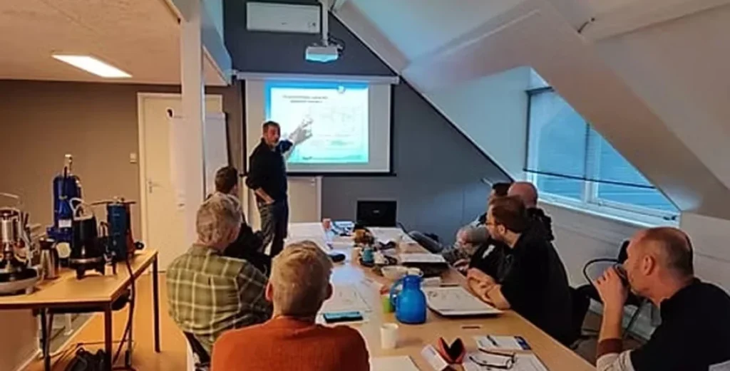 Deelnemers volgen aandachtig een presentatie tijdens een elektra-training in een klaslokaal met projectiescherm.