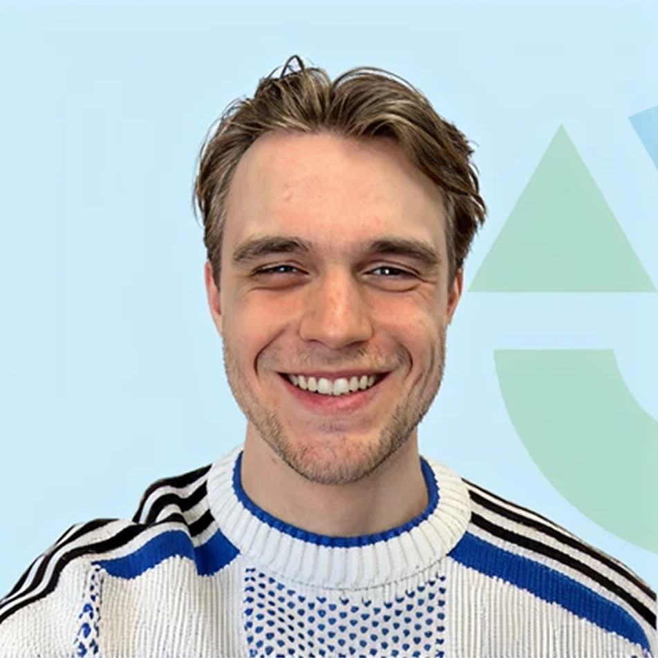 Loek Schuurman staat glimlachend met een wit en blauw gestreepte trui voor een lichte achtergrond.