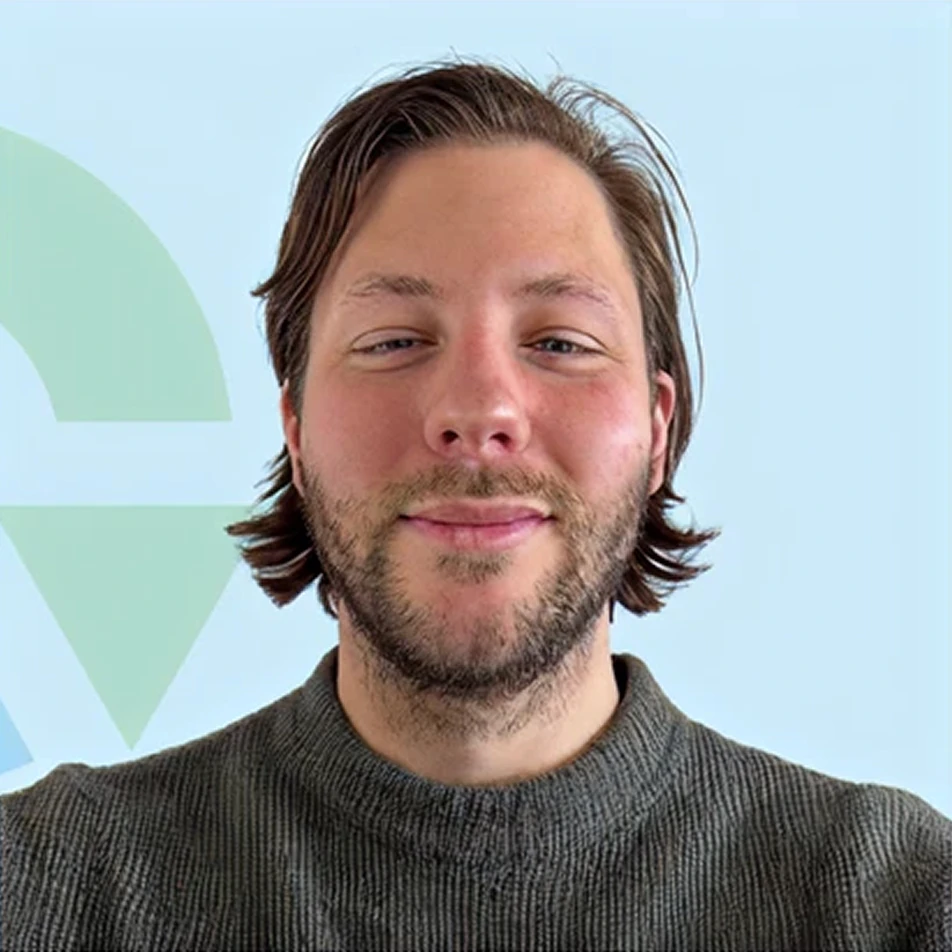 Thomas Kevel werkt bij Kennis van Pompen. Hij heeft halflang haar en een baard die naar de camera lacht, tegen een achtergrond met een zacht patroon en lichte kleuren.