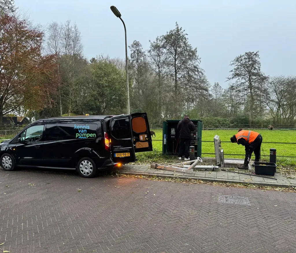 Technici van "Kennis van Pompen" werken aan een installatie in een groene landelijke omgeving.
