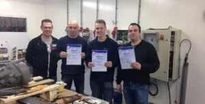 Vier mannen poseren trots met hun diploma's na het succesvol afronden van een technische training in een opleidingscentrum.